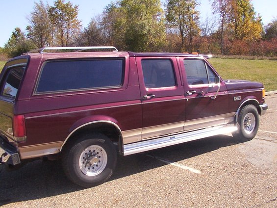 Maroon extended cab pickup truck with a camper shell, tan lower trim, and chrome running boards