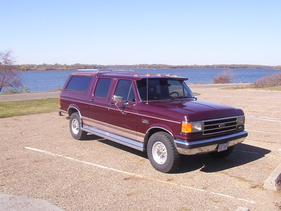Maroon Ford C-350 Centurion conversion van parked by a lake, 3q-front view