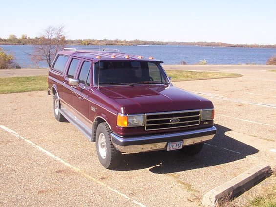 Maroon Ford SUV conversion with camper shell, parked by a lake