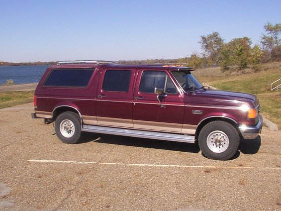Maroon Ford SUV conversion with tan trim, parked by a lake