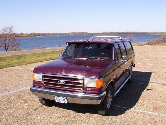 Maroon SUV with a roof rack and sun visor parked by a lake