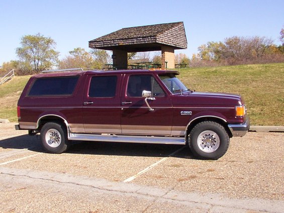 Maroon SUV with tan trim and roof rack parked on gravel lot