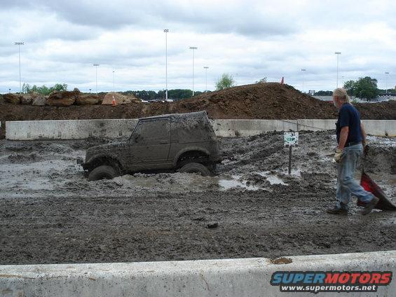 1988 Suzuki Samurai stuck deep in mud with a person walking nearby