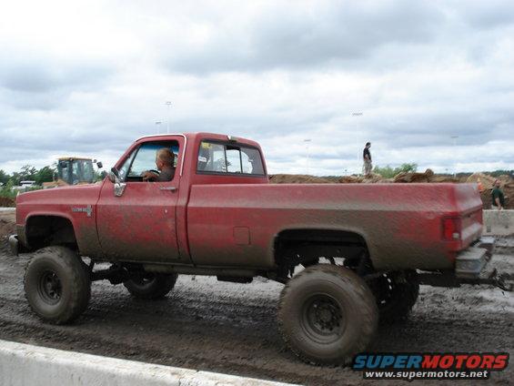 red pickup truck with big tires driving through mud