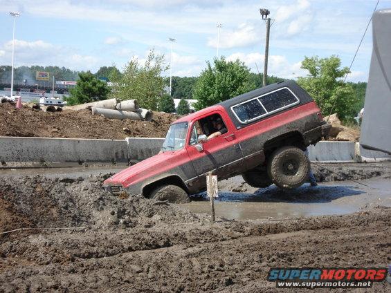 Red and black SUV with lifted suspension stuck in mud, driver visible