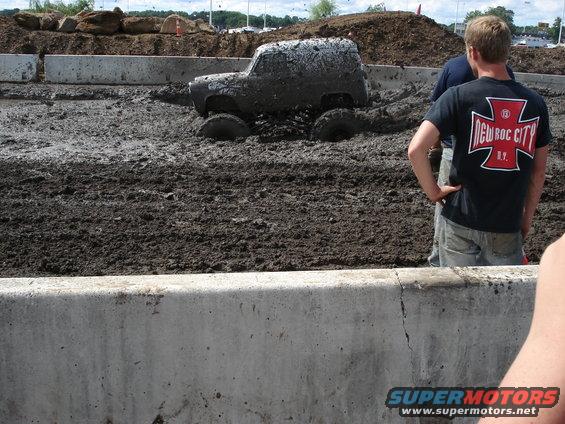 Off-road vehicle partially submerged in thick mud, with spectators watching