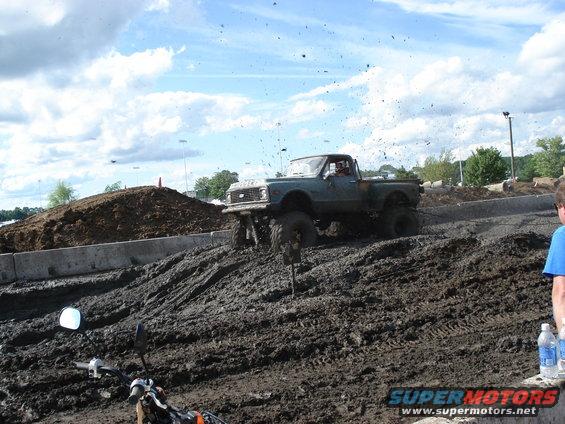Lifted pickup truck driving through mud, kicking up dirt