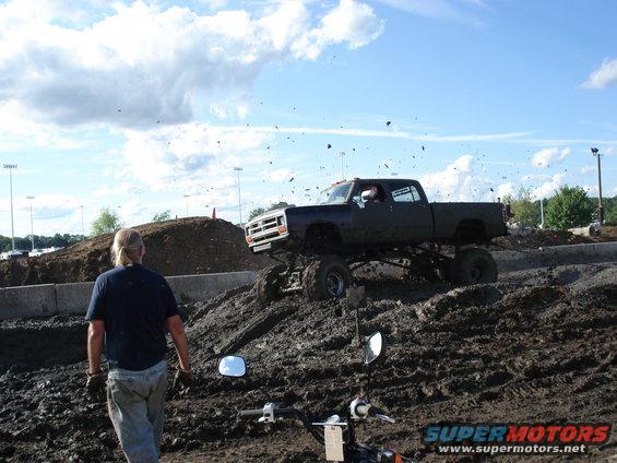 lifted pickup truck driving through mud, person watching