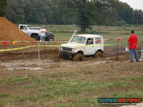 White 1988 Suzuki Samurai stuck in mud pit with people watching