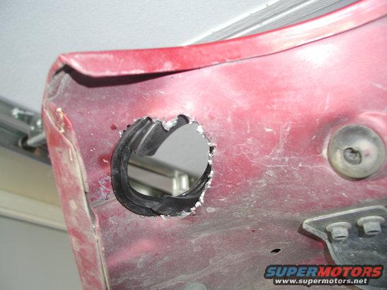 close-up of a red vehicle body panel with a rough hole cut into it, rubber grommet visible inside the hole
