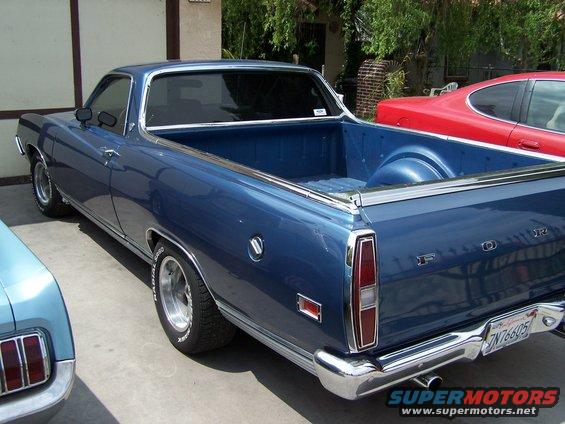 Blue pickup truck parked next to a red car and a light blue car. Rear view shows chrome bumper and taillights