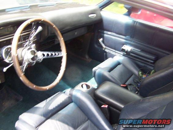 Car interior with wood-rimmed steering wheel, dark blue seats, and center console