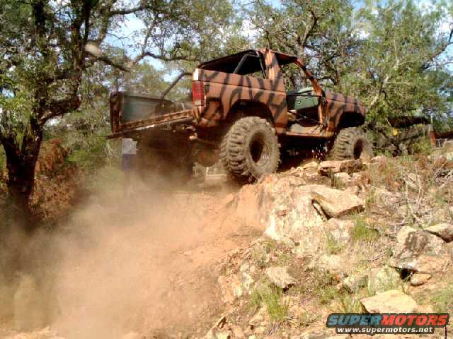 off-road vehicle with tiger stripe paint climbing a rocky dirt hill, kicking up dust