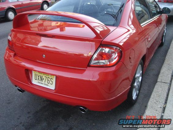Rear view of red Dodge Neon with spoiler and dual exhaust. Another red car is parked behind it