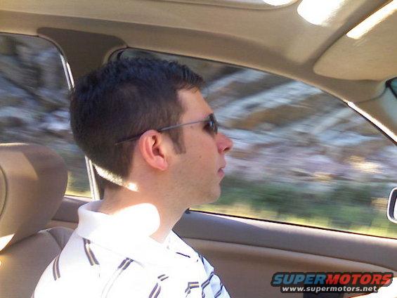 Man wearing sunglasses driving a car, looking out the passenger window