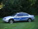1999 Ford Taurus - A silver 1999 Ford Taurus sedan with custom blue flame decals and chrome wheels is parked on a grassy lawn in front of trees.