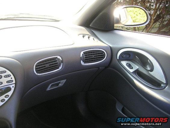 Interior shot of a car's dashboard and door panel, showing air vents and a door handle with carbon fiber trim
