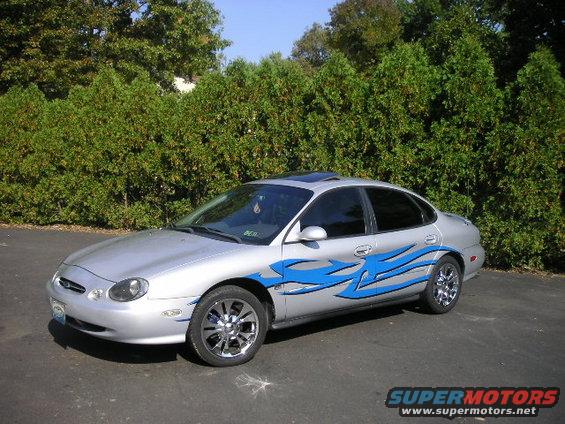 Silver 1999 Ford Taurus with blue flame decals and chrome wheels