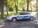 1999 Ford Taurus - A silver sedan with custom blue flame decals is parked on a paved surface with trees and houses in the background.
