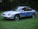 1999 Ford Taurus - A silver sedan with blue flame decals is parked on a grassy lawn with trees in the background.