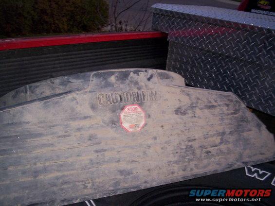 Radiator fan shroud with 'CAUTION FAN' and 'STOP DO NOT TOUCH' labels. It's in the bed of a pickup truck next to a toolbox