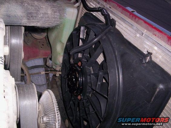 Engine bay view of a black electric cooling fan and radiator with a green fluid reservoir