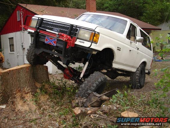 1989 Ford Bronco with lifted suspension and off-road tires climbing over a large tree stump
