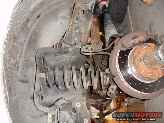 Close-up of a vehicle's front suspension, showing the coil spring, shock absorber, brake rotor, and caliper