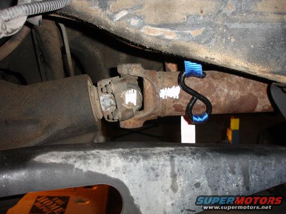 Close-up of a vehicle's driveshaft with a blue strap attached to the exhaust pipe
