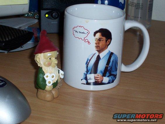 Mug with a picture of a man in a blue shirt and suspenders holding a cup, with a thought bubble saying "Uh, Yeah...". A garden gnome is next to it