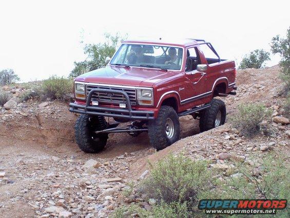 Red lifted Ford Bronco with aftermarket bumper driving on a dirt trail