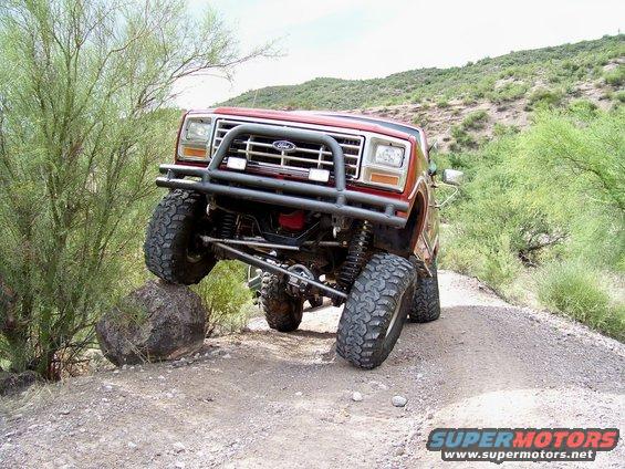 Red Ford Bronco with aftermarket bumper and large tires navigating a rocky trail