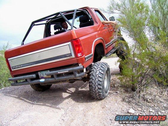 Red Ford Bronco with roll cage on a dirt trail, rear view