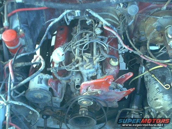 Engine bay with red valve covers and distributor cap. Wires and hoses are visible