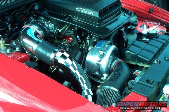 Red 2006 Ford Mustang engine bay with a Cobra supercharger and polished intake piping