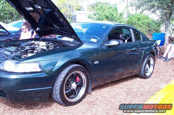 Dark green coupe with hood open, showing engine and red brake calipers on aftermarket wheels