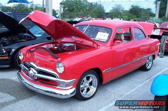 Red 1949 Ford Coupe with hood open, chrome grille, and custom wheels