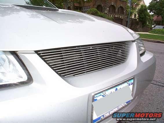 Front of a silver car with a horizontal chrome grille and a license plate