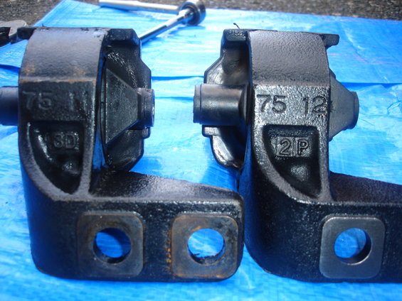 Two black metal engine mounts with numbers stamped on them, resting on a blue tarp
