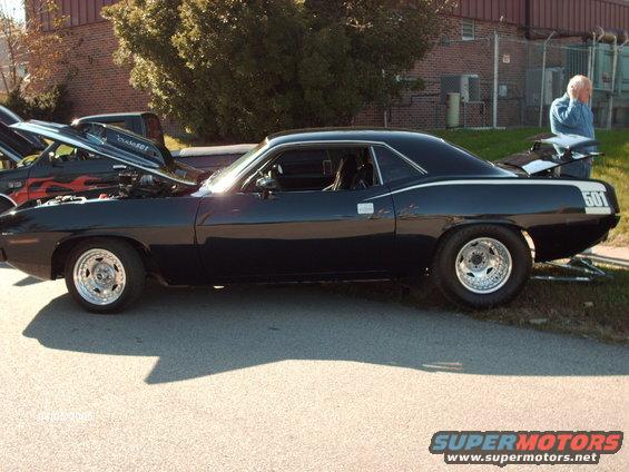 Black 1970 Plymouth Barracuda with racing stripes and number 501 on the rear quarter panel. Another car with its hood up is to the left