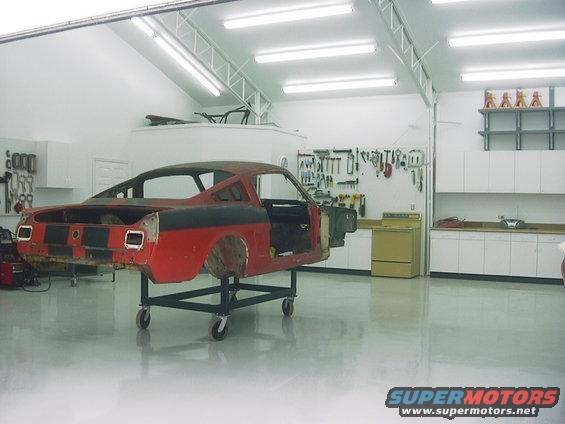 1967 Ford Mustang fastback body on a rolling stand in a garage, stripped down for restoration
