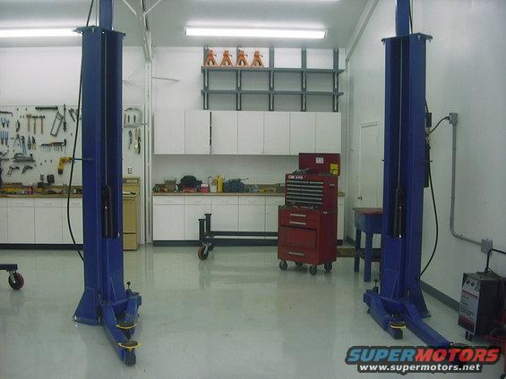 Two-post car lift in a garage with tool chests and shelves