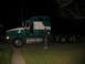 1988 Ford C-350 (Centurion Conversions) - Man stands next to a green and white semi-truck tractor parked on a grassy area at night.