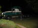 1988 Ford C-350 (Centurion Conversions) - A person stands next to a semi-truck tractor at night, with some text visible on the side of the cab.