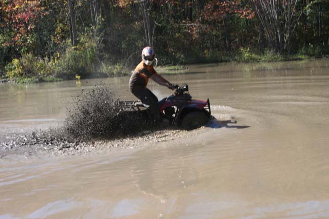 Red ATV splashing mud while riding through water