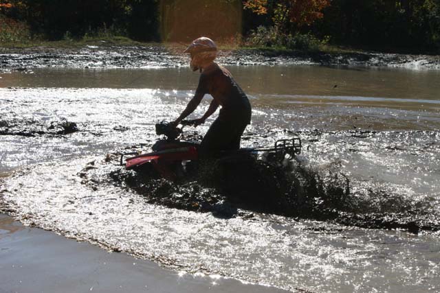 Person on ATV splashing through muddy water, wearing a helmet