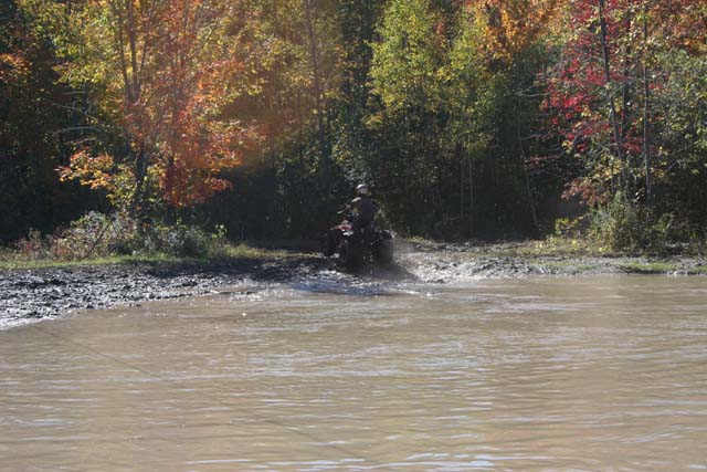 ATV driving through muddy water with trees in background