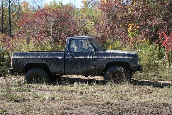 Side view of a black pickup truck stuck in mud with off-road tires