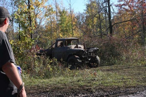 Mud-covered pickup truck with roll cage parked in wooded area during autumn