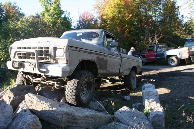 Lifted 1979 Ford F-Series pickup truck with bull bar, navigating rocks. Another truck is visible in the background